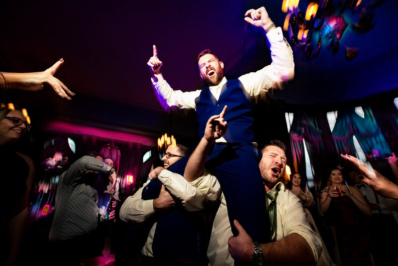 A groom being lifted in the air with his hands in the air at the Toledo Club