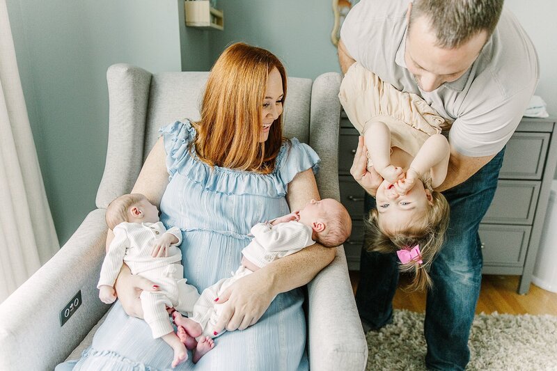 mom holds twins and dad holds toddler upside down during in-home newborn photo session with Sara Sniderman Photography in Natick Massachusetts