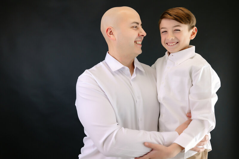 Dad stands holds and smiles at his son