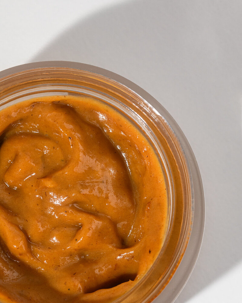 Close-up photo of a jar of facial peel. It's in a glass jar and orange in color.