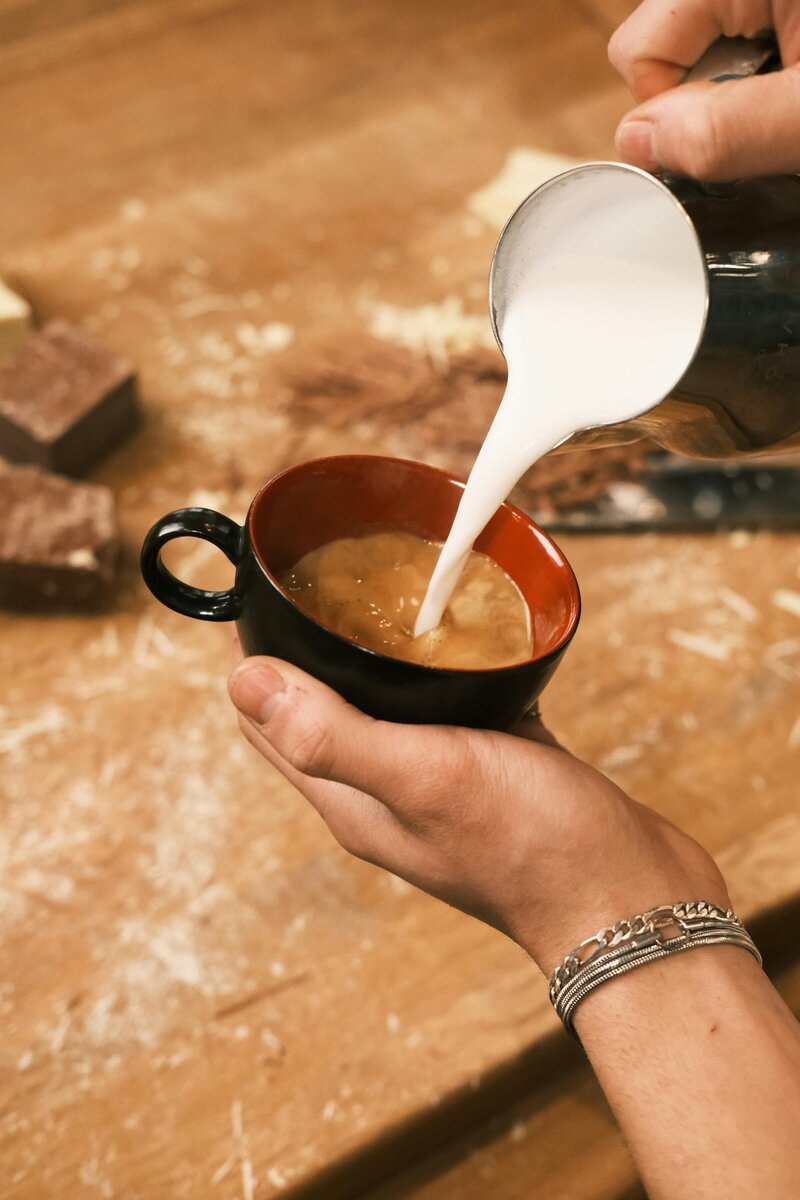 hands pouring frothed milk into a cup of espresso