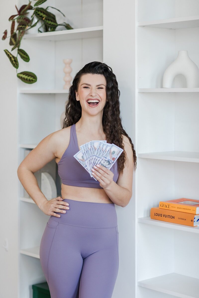 A photo of Hailey Ann, a bookkeeper and somatic Money coach for female entrepreneurs professional headshot holding money