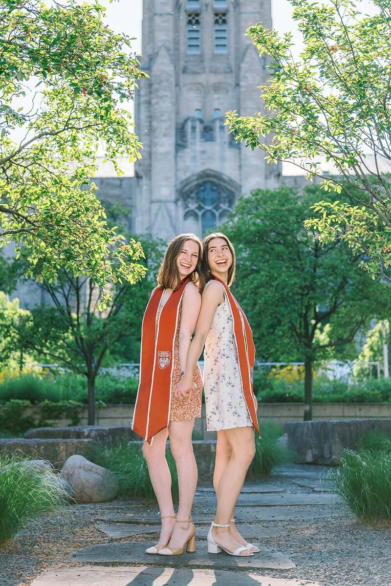 Two University of Chicago graduates back to back in front of Rockefeller Chapel for their cap and gown photos