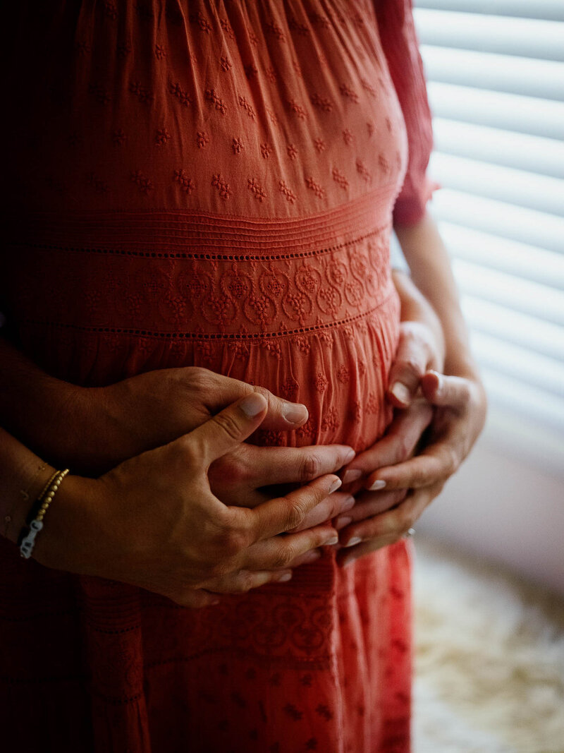Two pairs of hands hold a pregnant belly.