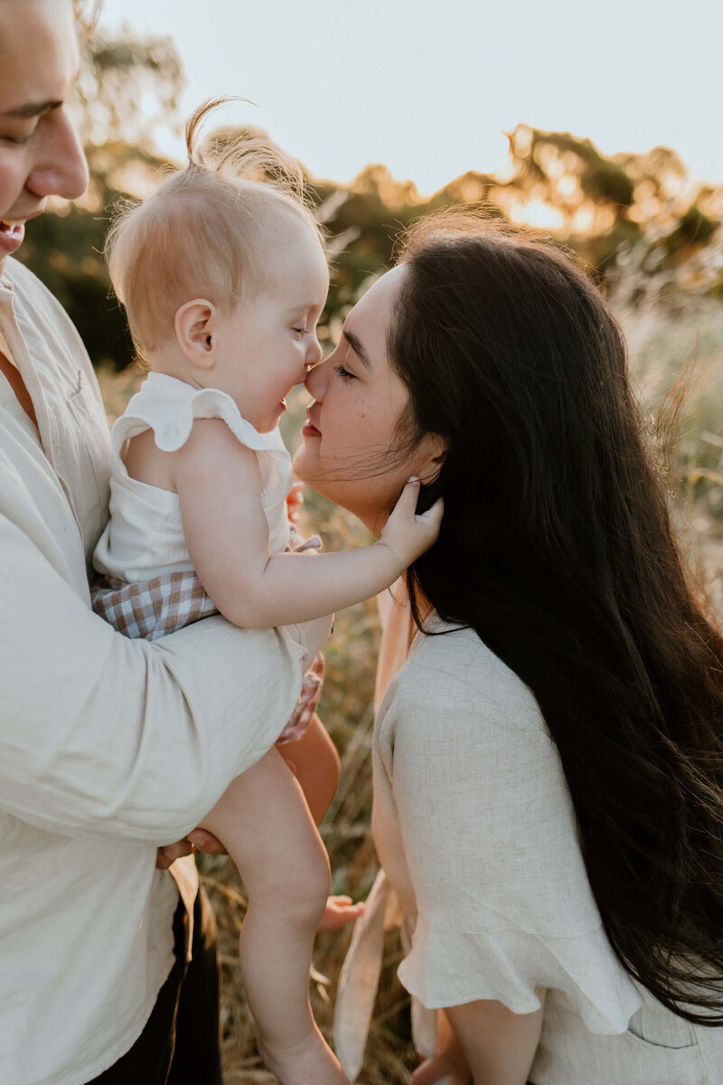 Photo of a mother leaning in for a kiss with her toddler at sunset