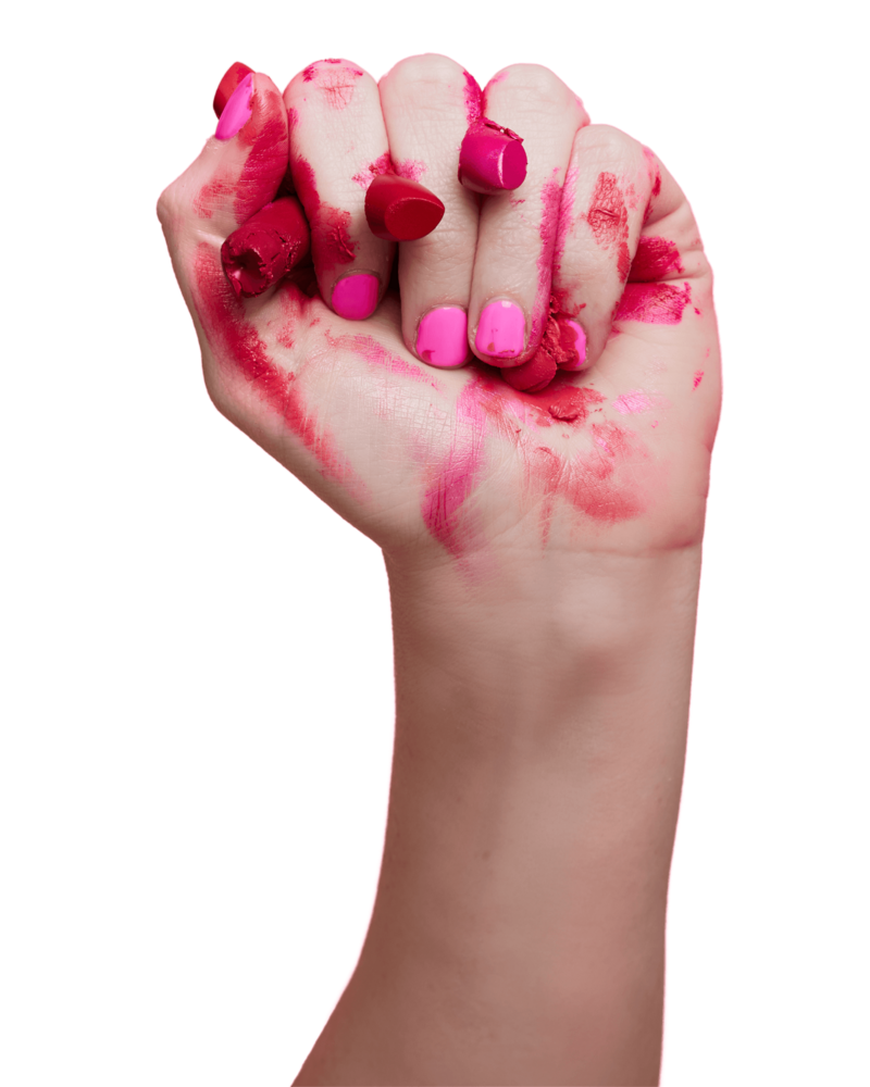 A fist holding holding red and pink crushed lipsticks.