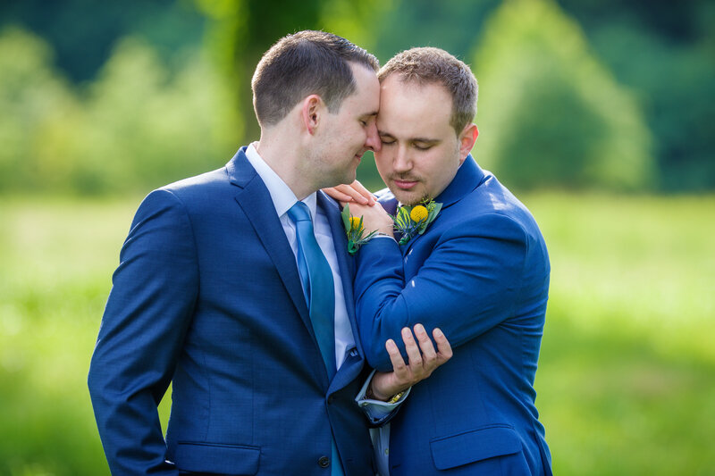 Grooms sharing a tender embrace during their first look at Pen Ryn Mansion, capturing a heartfelt wedding moment.