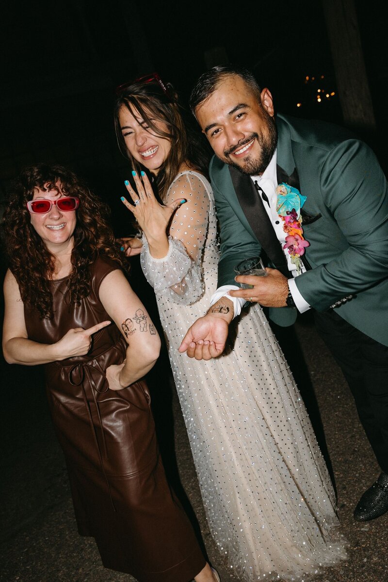 A bride and groom stand with their wedding planner showing off the custom temporary tattoos on their arms