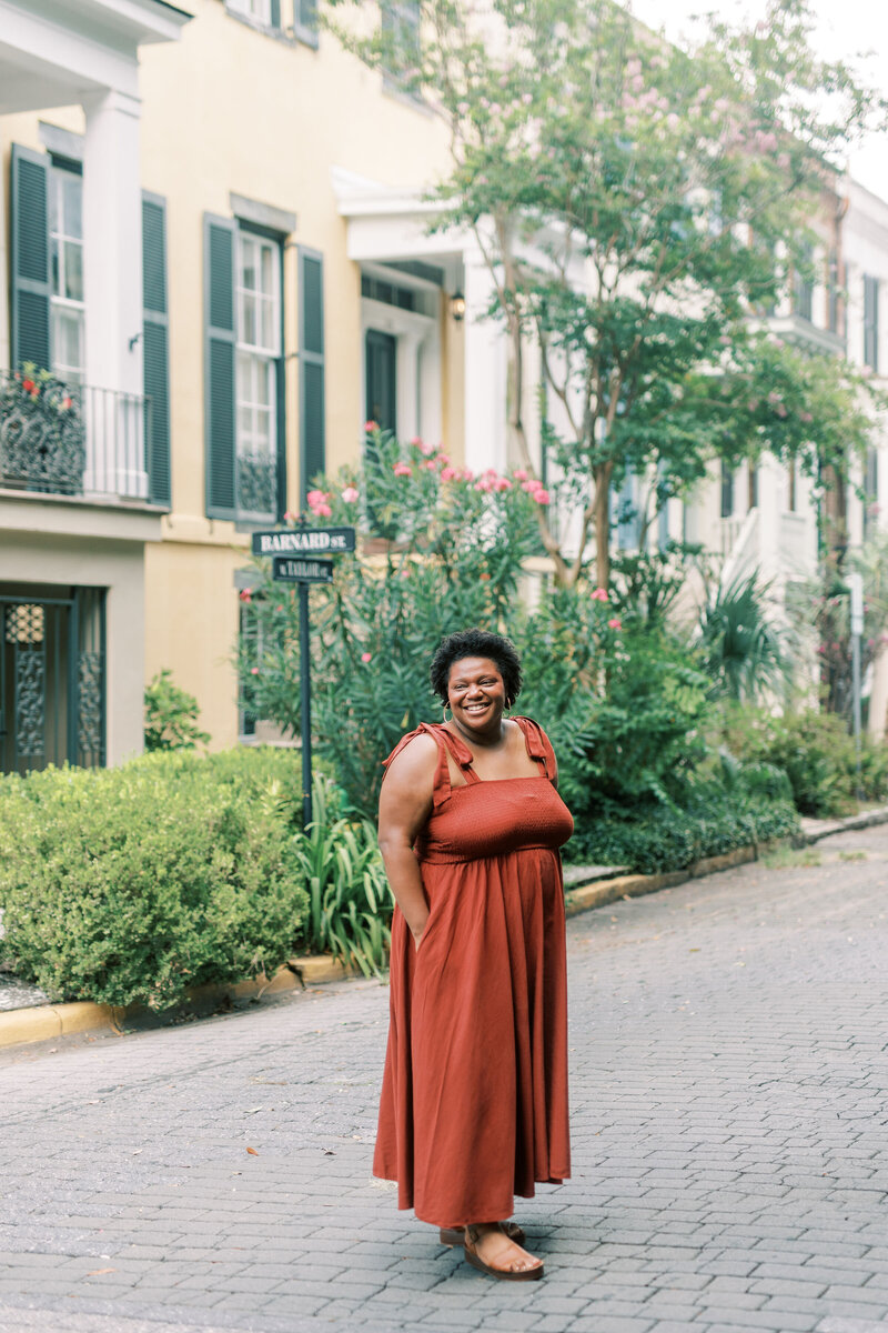 Portrait of Grey Cove Designs founder smiling in a rust-colored dress on a charming cobblestone street in Charleston, SC, with styling inspired by the timeless architecture and lush greenery of Charleston, South Carolina, Savannah, Georgia, and Amelia Island, Florida.
