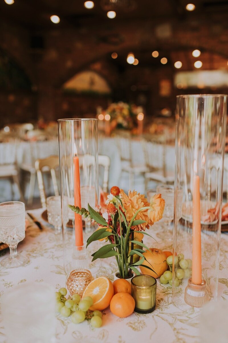 Elegant reception table with orange flowers, fresh fruit, and tall glass candle holders, set for a wedding reception in the century room at grbic events in st. louis