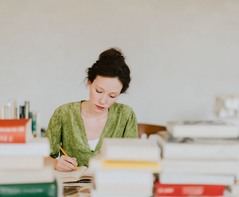 Creative client testimonial of a woman writing in green blouse surrounded by books, captured during luxury branding masterclass with Jasmina Kimova