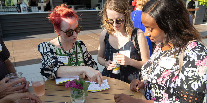 Three women standing around an outdoor table at a corporate event