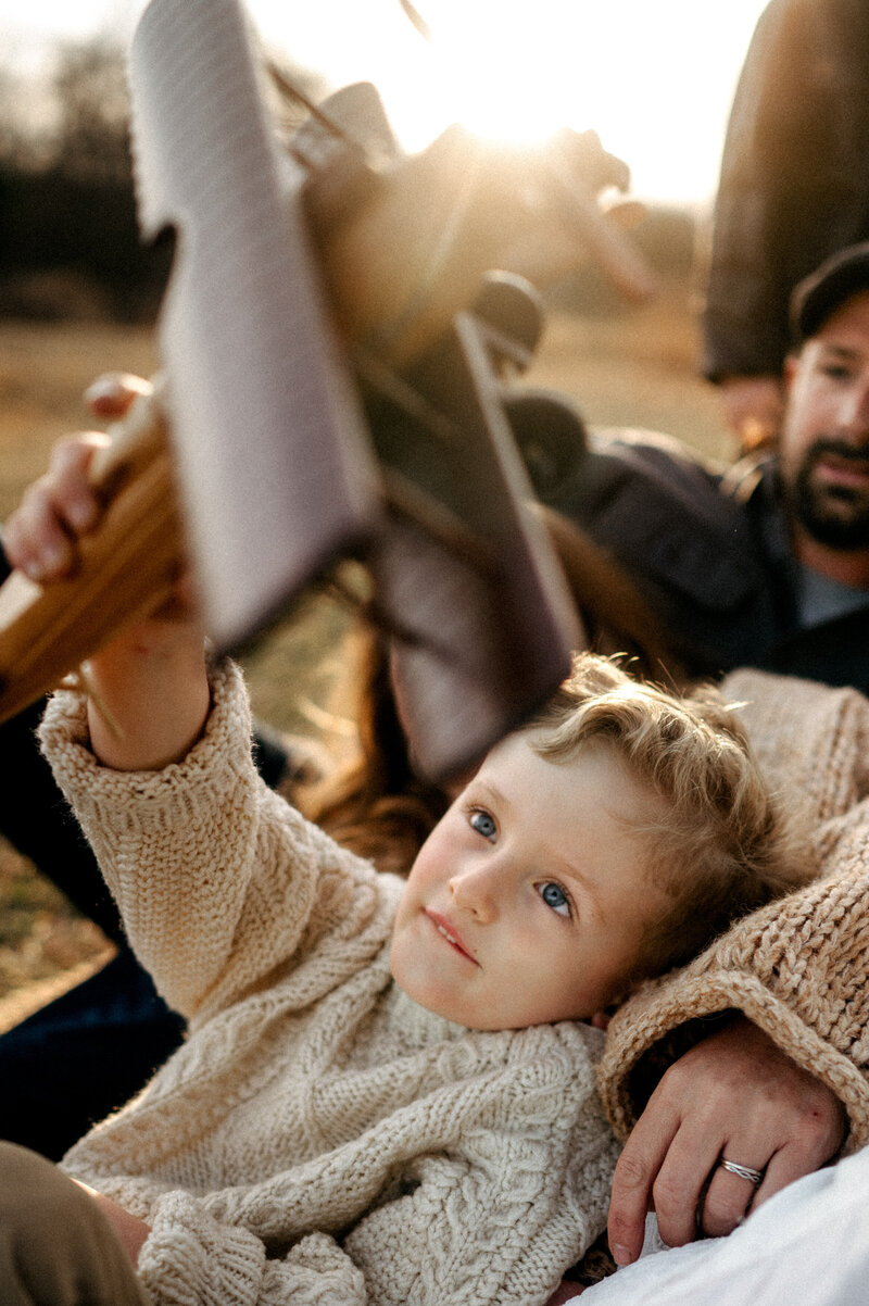 A mother in a gorgeous floral gown holding her toddler while the sun sets behind them. 