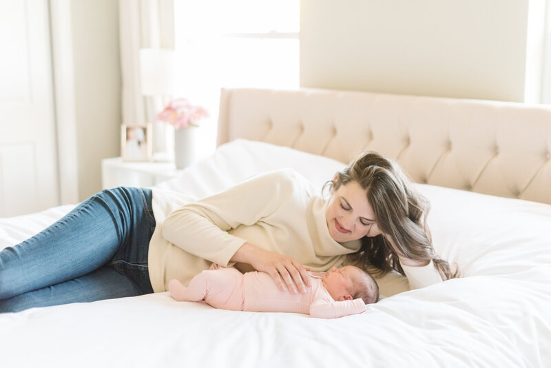 Mother in cream sweater laying on bed looking down at newborn baby - Washington DC Newborn Photographer