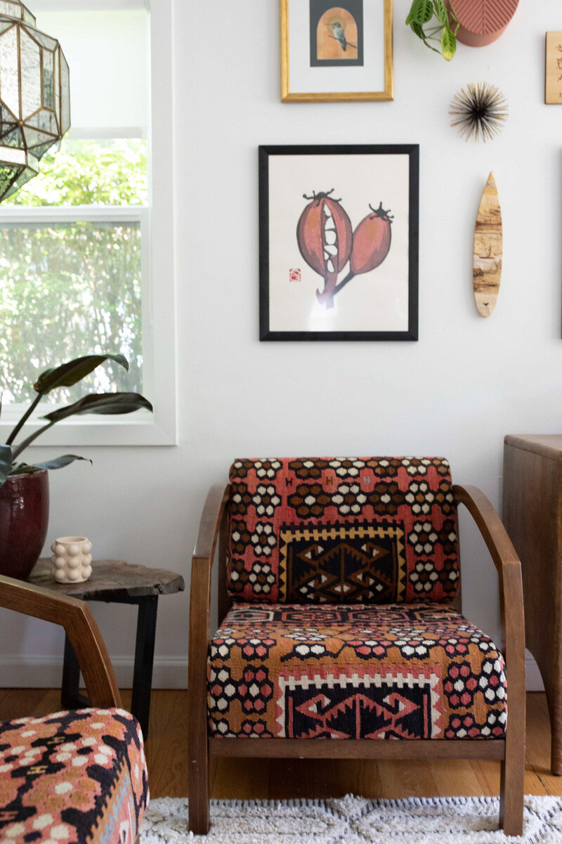 Seating area featuring organic modern chairs with patterned fabric, a wooden side table with a houseplant, and decorative art on the wall.