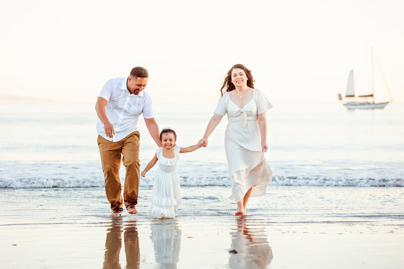 Happy family running along the shore in Avila Beach, CA with Fresno Family photographer One Good Shot Photography