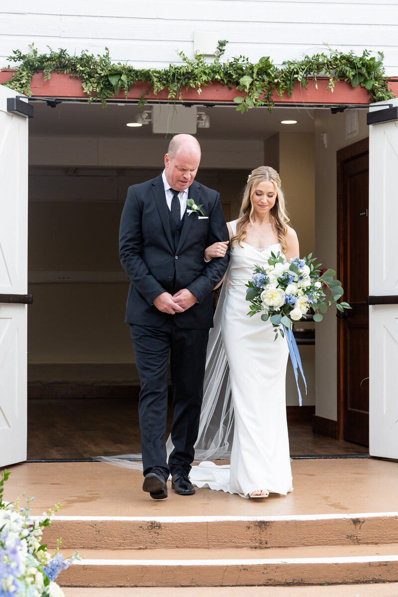 Spring wedding at WinMock at Kinderton, designed by Charming Carolina — bride walking through the double doors onto the East Terrace with floral-lined aisle and open-air ceremony setup.