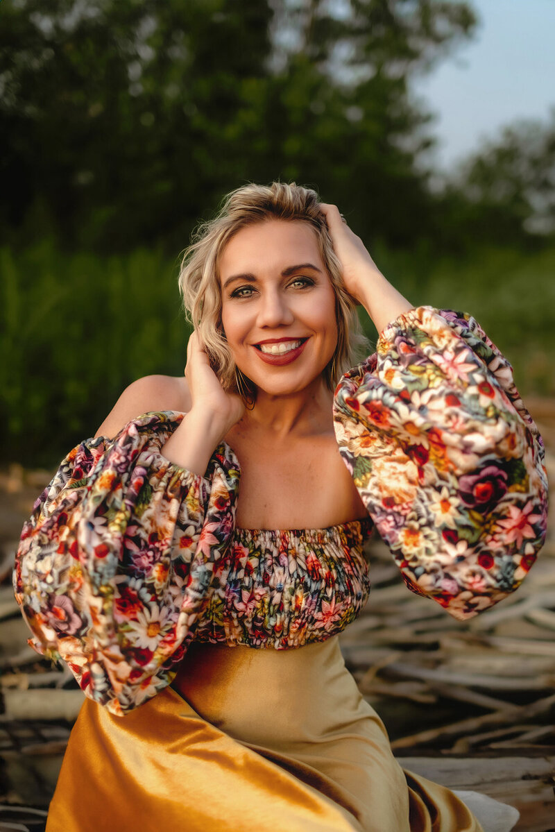 Photographer Michelle Gritters sits outside at sunset in a colorful floral blouse and gold skirt