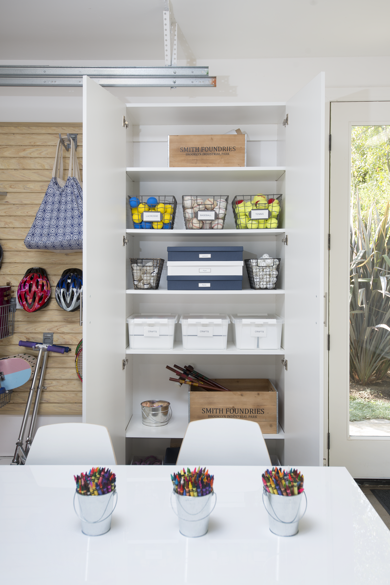 Open custom cabinet in a garage with bins full of sport equipment and labeled boxes with craft supplies