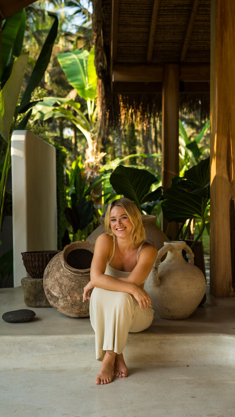 yoga woman sitting smiling amongst plants and large vases