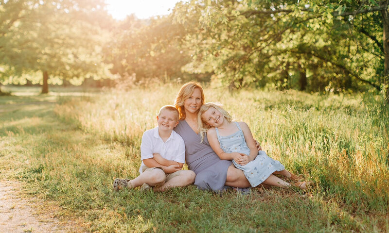 A mother and her two kids sitting in a  fieldof green grass
