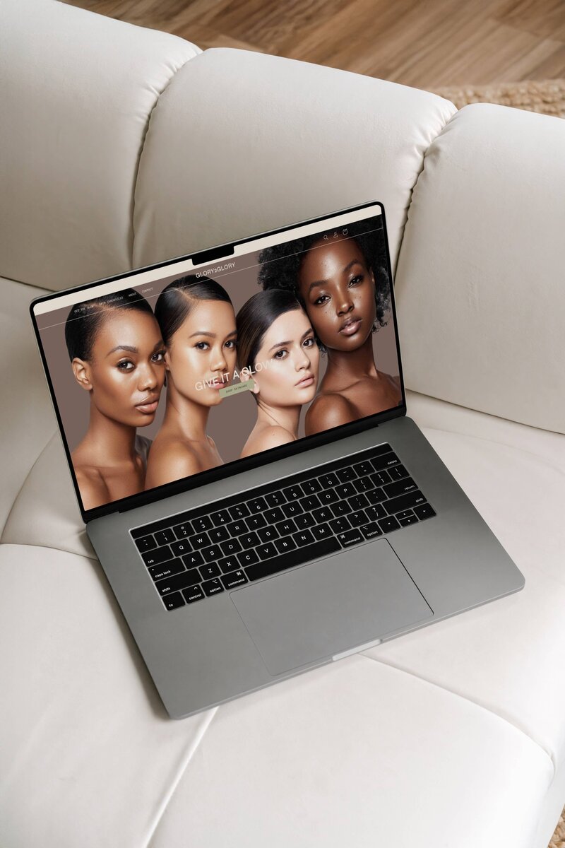 Glory2Glory website homepage showcased on an open Macbook Pro laptop sitting on top a cream couch