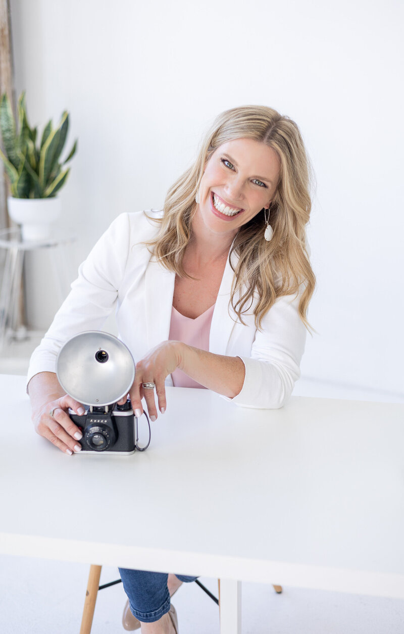 Woman headshot sitting holding a vintage camera and smiling at the camera