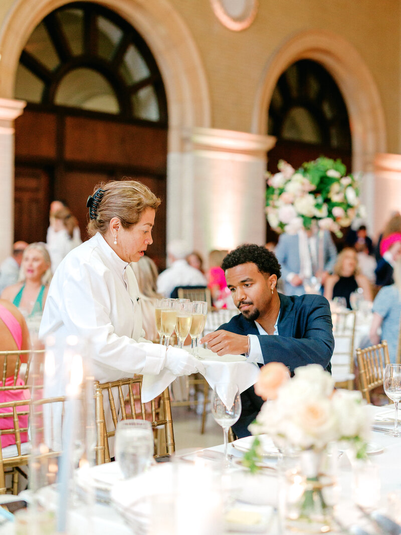 A waitstaff member serves a wedding guest a glass of champagne at the beginning of a wedding reception.