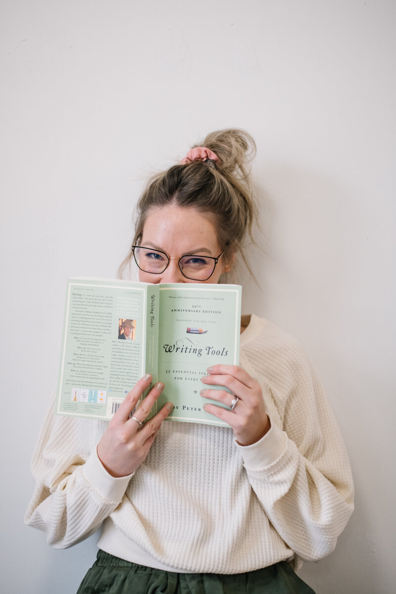 Sammy with glasses and a messy bun holding up a Writing Tools book