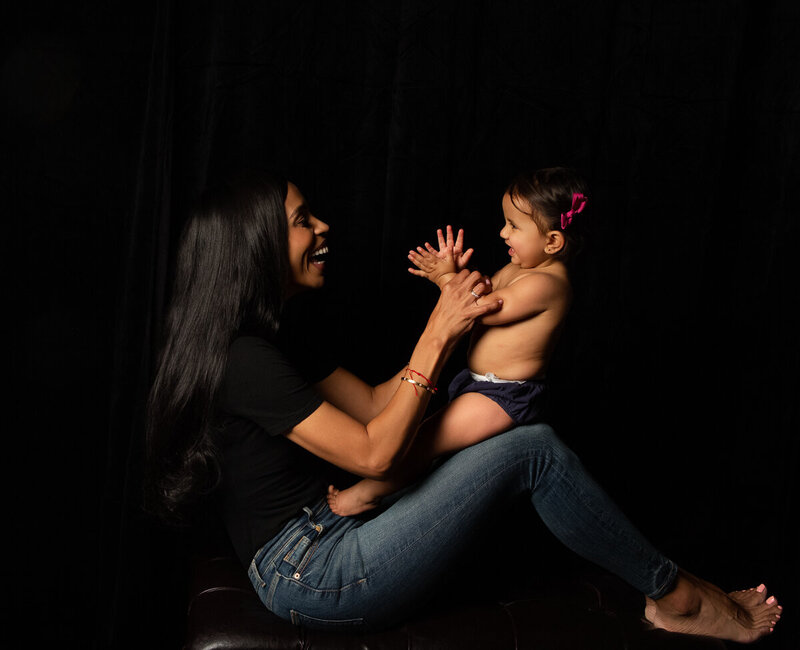 Charlotte NC toddler photography one year baby girl clapping and laughing looking at her smiling latino mother 2024