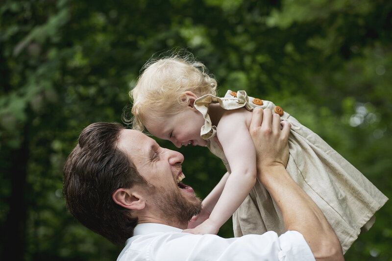 A dad laughs as he picks up his young daughter and throws her up in the air