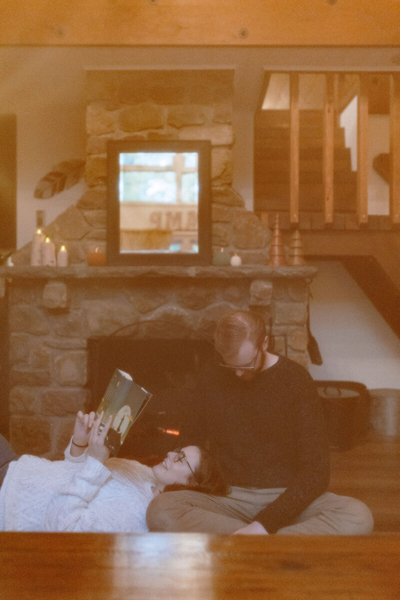 A man and woman relax on the floor, surrounded by the warm glow of a fireplace, creating a cozy and intimate atmosphere.