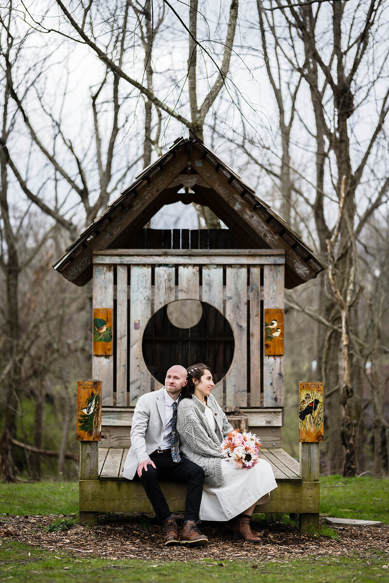 A couple sit on the edge of a bench that is attached to large, birdhouse like structure.