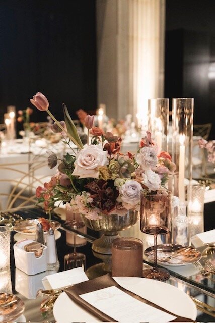 Floral centerpiece in soft mauve tones in a gold compote to and matching place settings. 