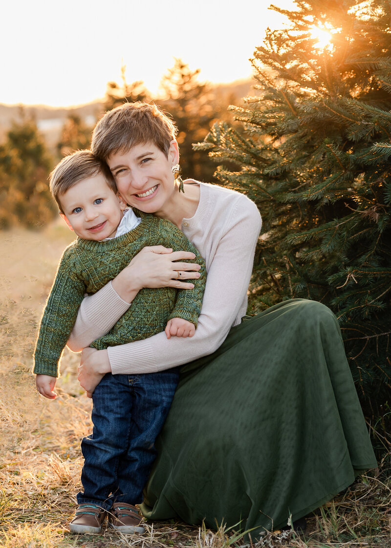 Lifestyle portrait of a mother and son hugging at a Christmas tree farm during golden hour.