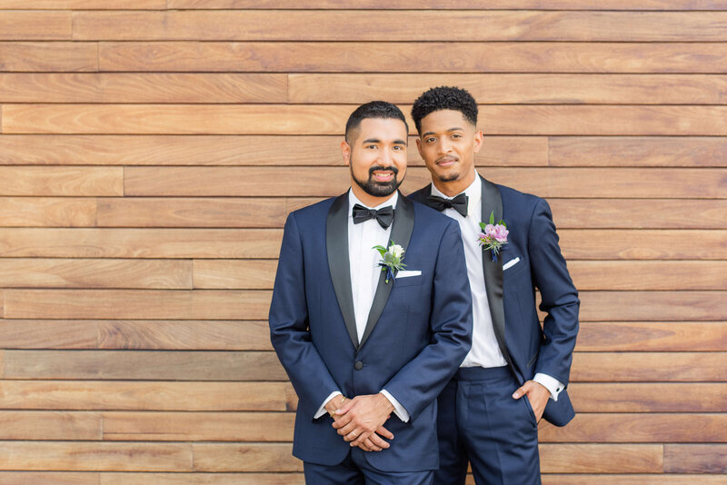 groom and groom posing in front of wood wall