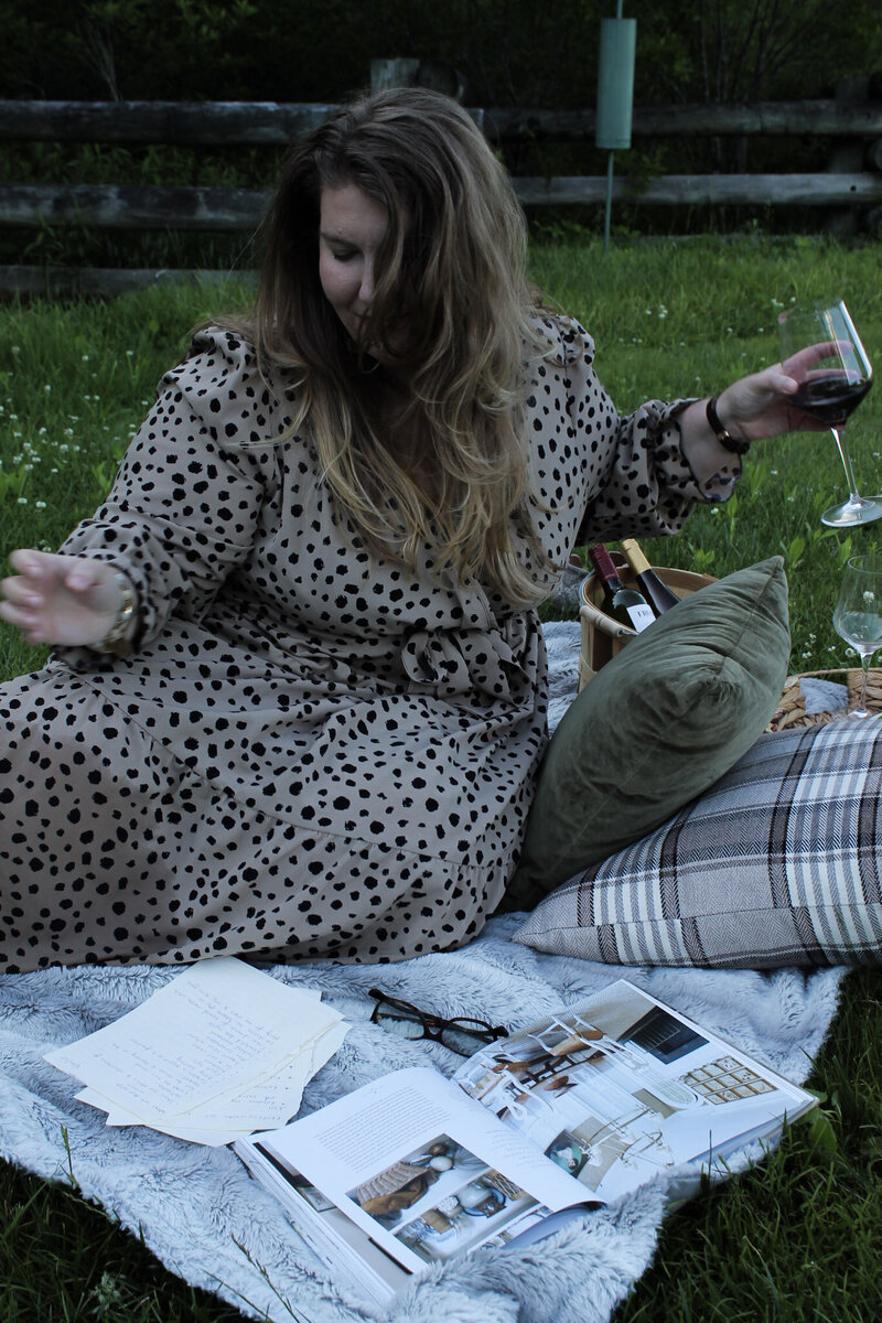 Ashleigh Henry, coach and founder, photographed in Asheville in black and brown dress — guiding women through the quiet unraveling of post-success life with red wine in hand and interior design books at her feet.