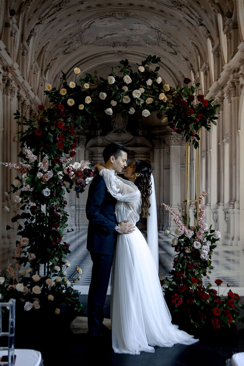 happy wedding couple at the ceremony hugging and kissing under the beautiful flower wedding arch