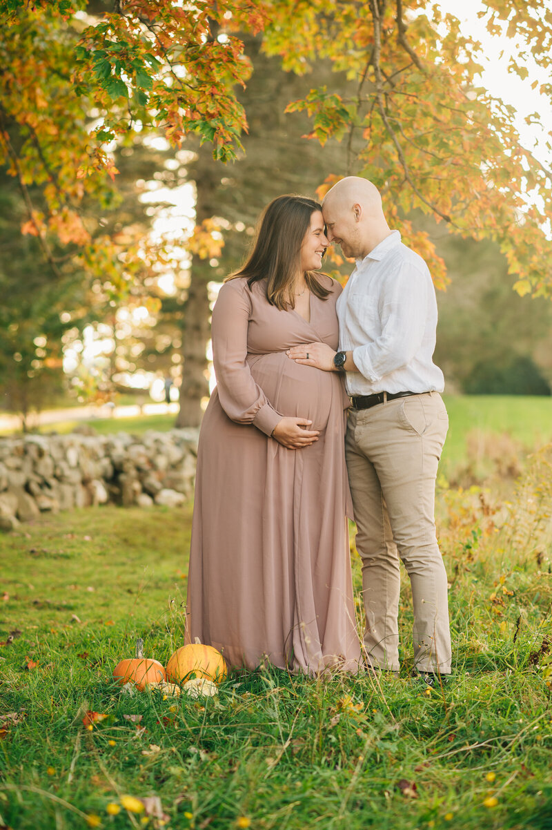 Couple in field, looking down at pregnant mom's belly