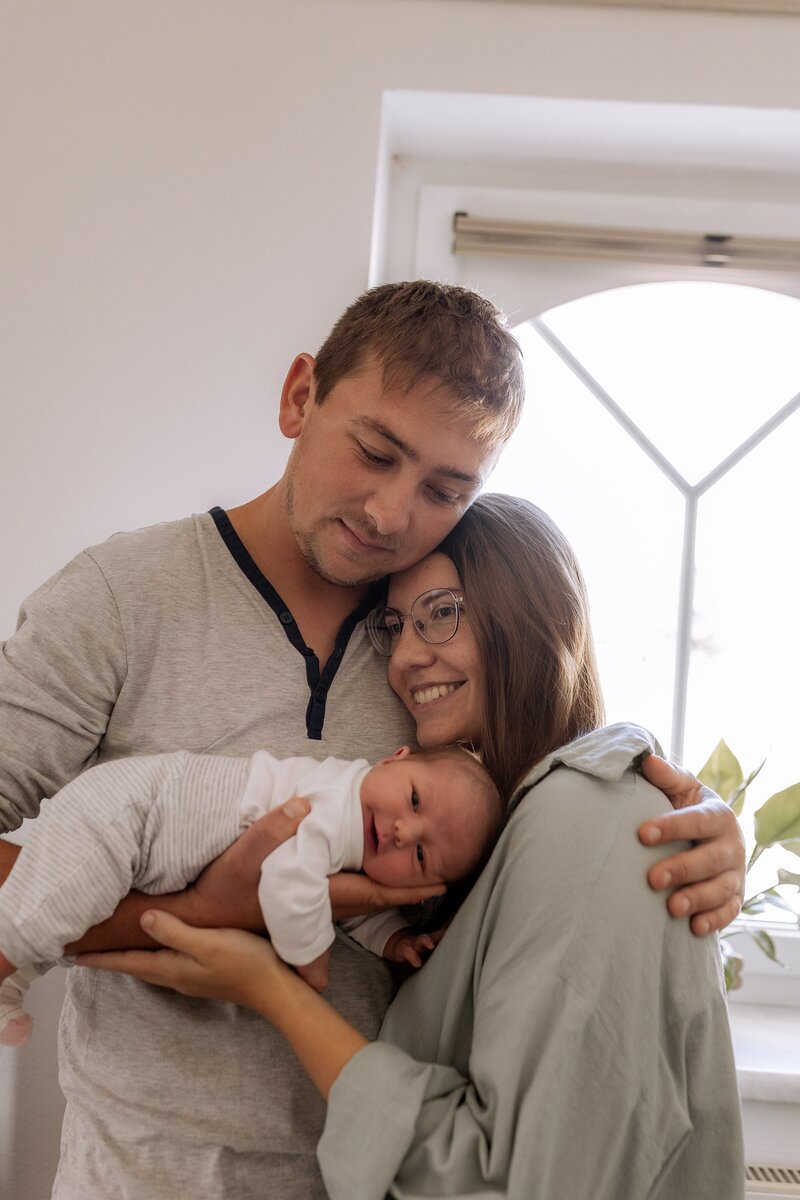 vater und Mutter halten sich und Baby im Arm