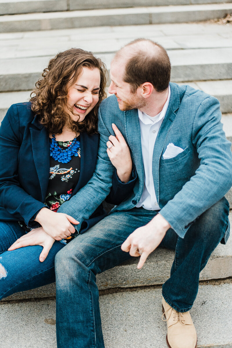 A couple sitting on stairs together laughing and holding each other's arms.