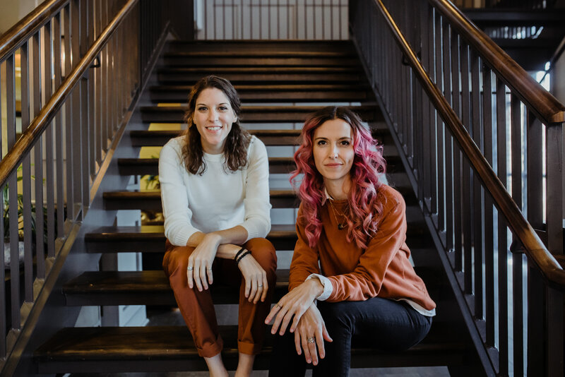 two women sitting on stairs smiling at the camera