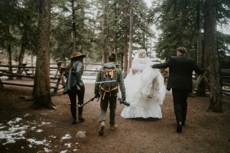 Couple walks with photo and video team through forest trail after Breckenridge wedding.