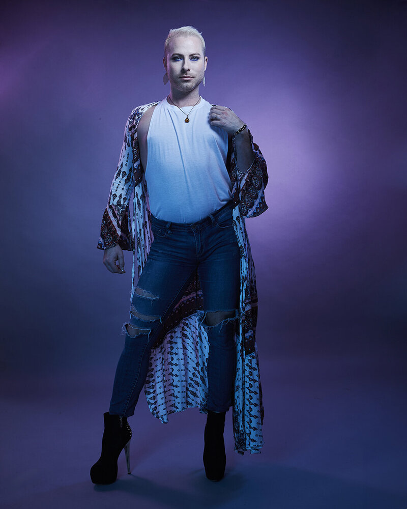 Dramatic full-body pose of Dain August in a blue sequined outfit, set against a vibrant studio backdrop, captured by Ylva Erevall.