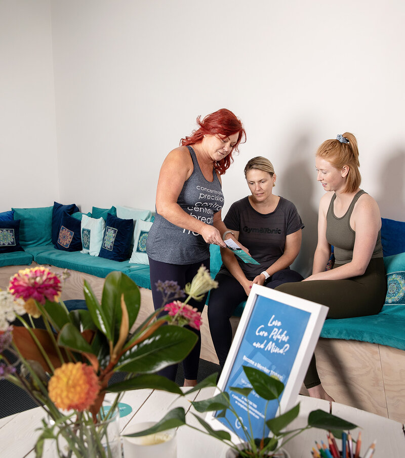 Fitness instructor showing brochure to clients in waiting room of pilates studio in Christchurch