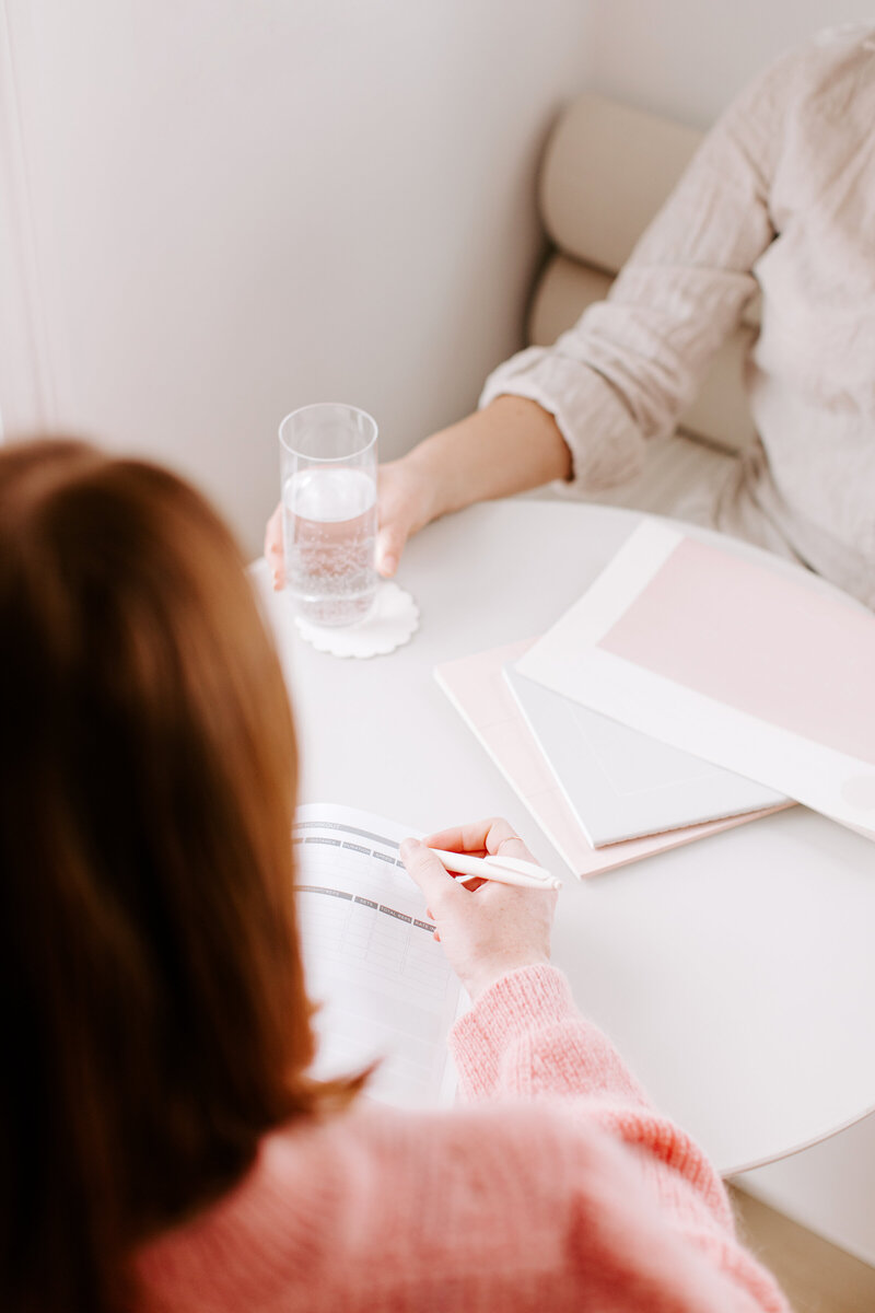 Health coach Jen taking notes during a coaching session with a client, demonstrating her commitment to personalized wellness and client support.