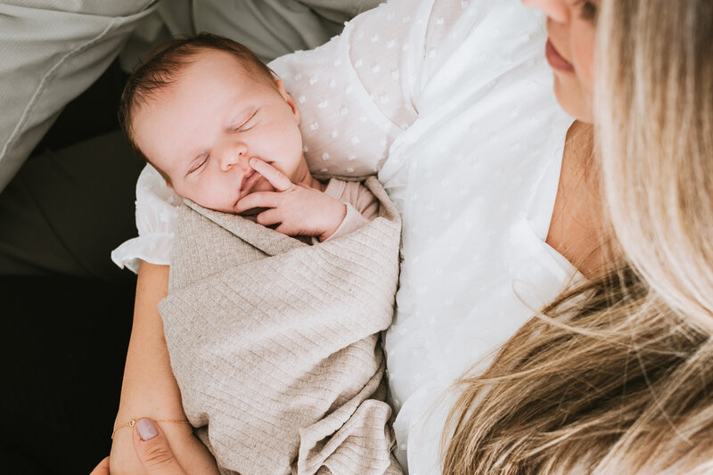 Mom wearing white while holding baby girl wrapped in tan blanket in their home in Davidsonville Maryland.