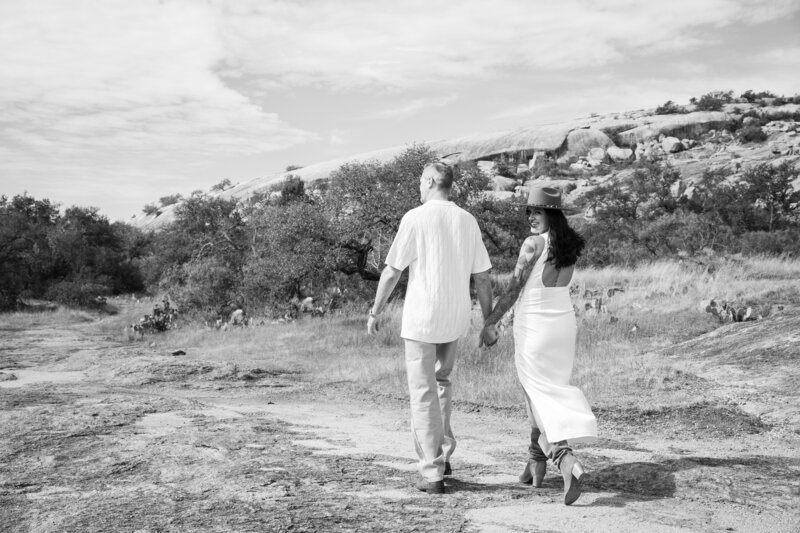 A black and white photo of a couple walking down a dirt road, captured by an Austin wedding photographer.