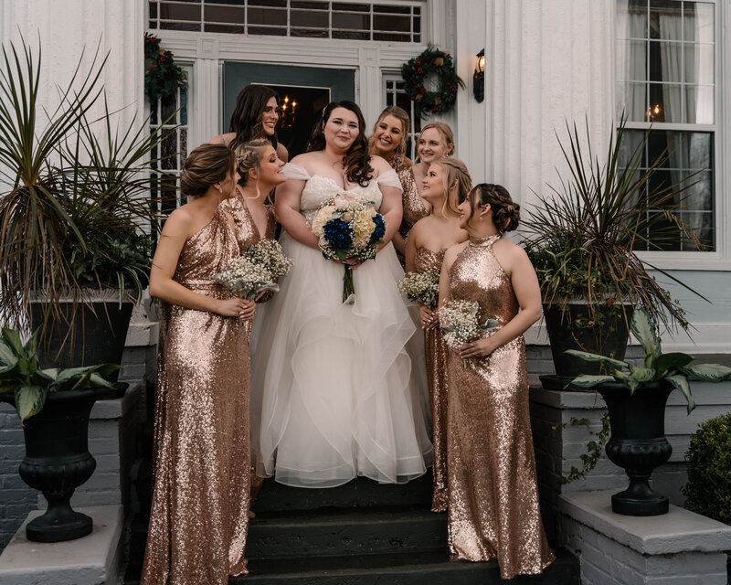 A beautiful bride and her bridesmaids standing together on the staircase of the Englund Estates Wedding Venue.