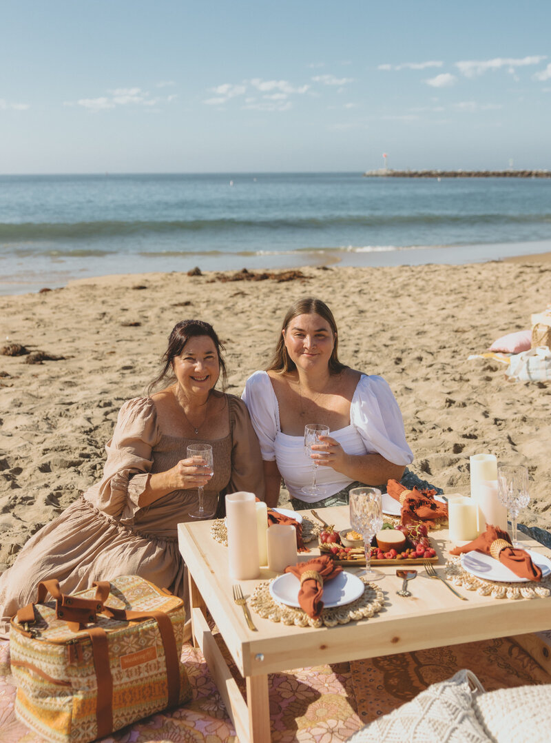Let's Picnic Co. - Two women sitting at a picnic table on the beach in Corona Del Mar California